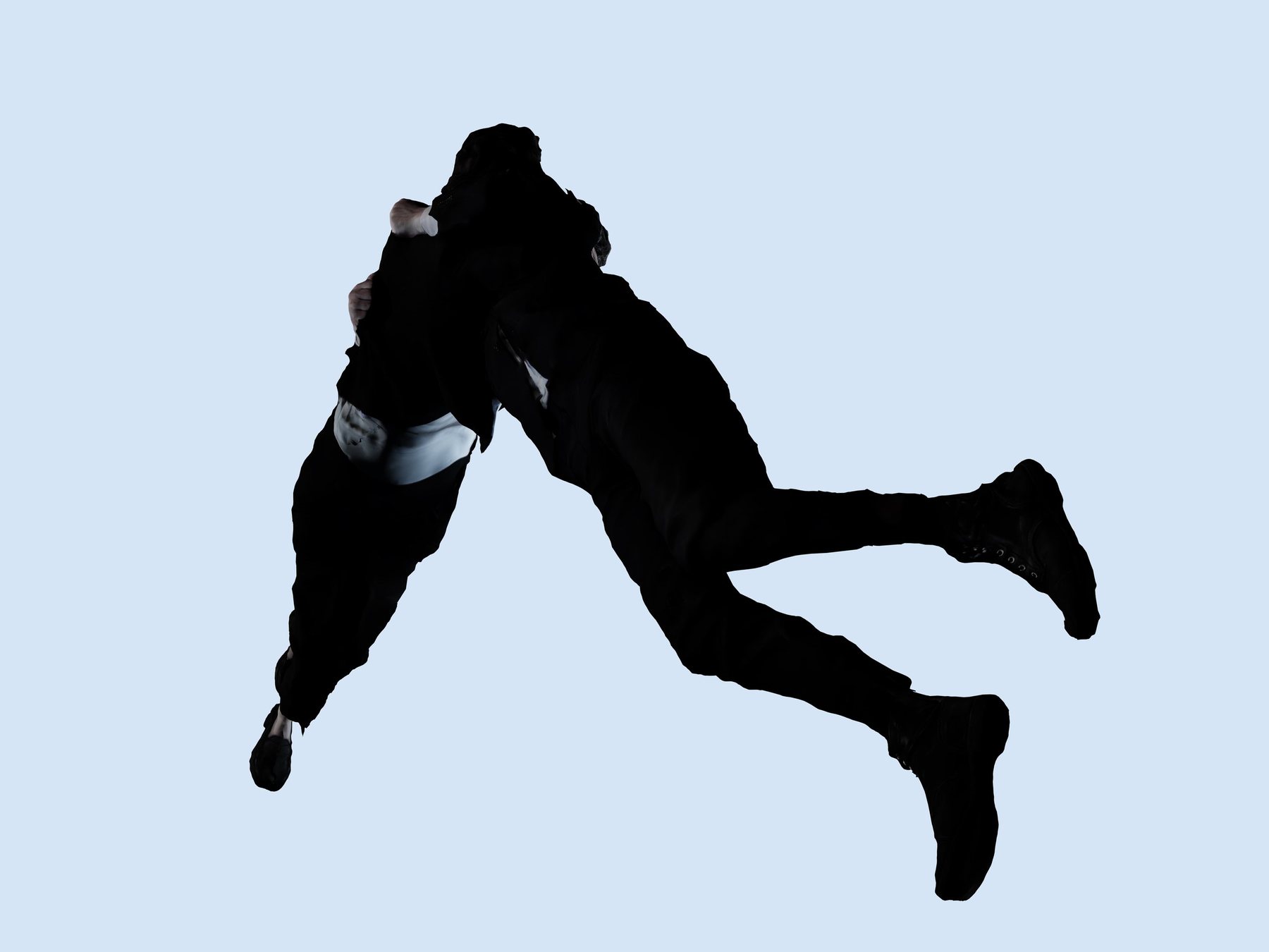 Two embracing figures in black, cut out against a pale blue background, caught mid-fall with boots and legs trailing.