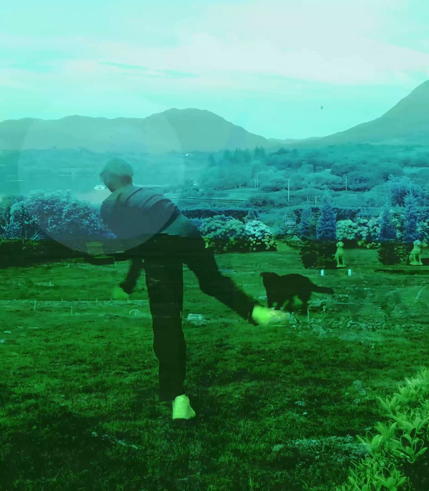 A boy kicks out across a green, hazy hillside as a black dog runs beside him; a translucent circle hangs over the scene. Still from And Then I Saw You Green (2022).