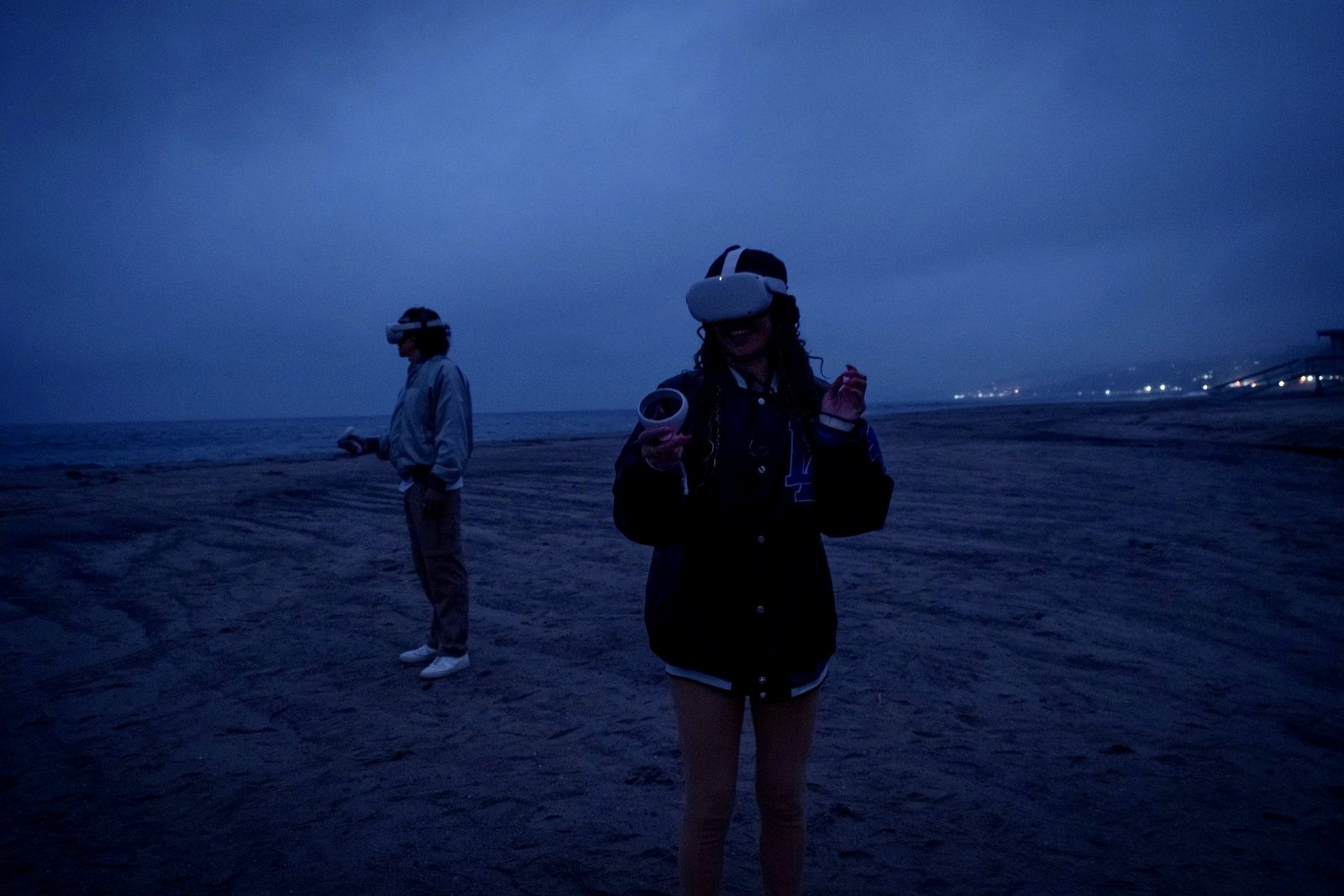Simulations: two participants in VR headsets stand on a beach at dusk, one smiling, the sea and distant lights behind them.