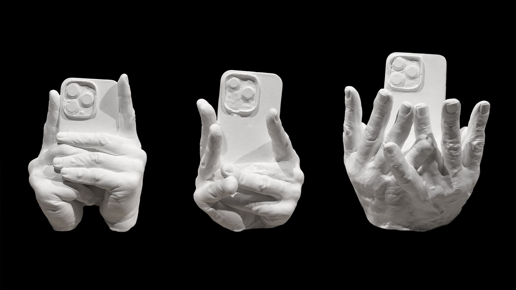 No End In Sight 137: Three white sculptures of hands holding smartphones, on a black background.