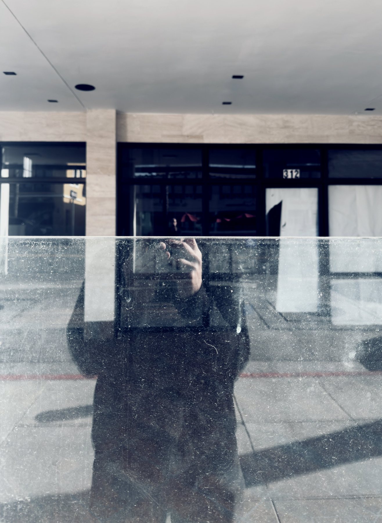 No End In Sight 138: The artist's reflection, with one hand raised, in a dusty glass pane in front of a building numbered 312.