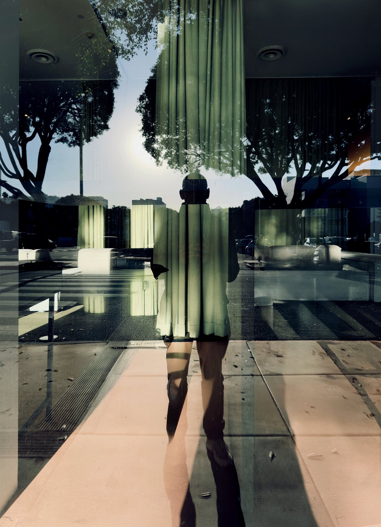 No End In Sight 128: The artist's shadowy silhouette cut by green vertical stripes of curtain reflected in glass, with a pink pavement and trees.