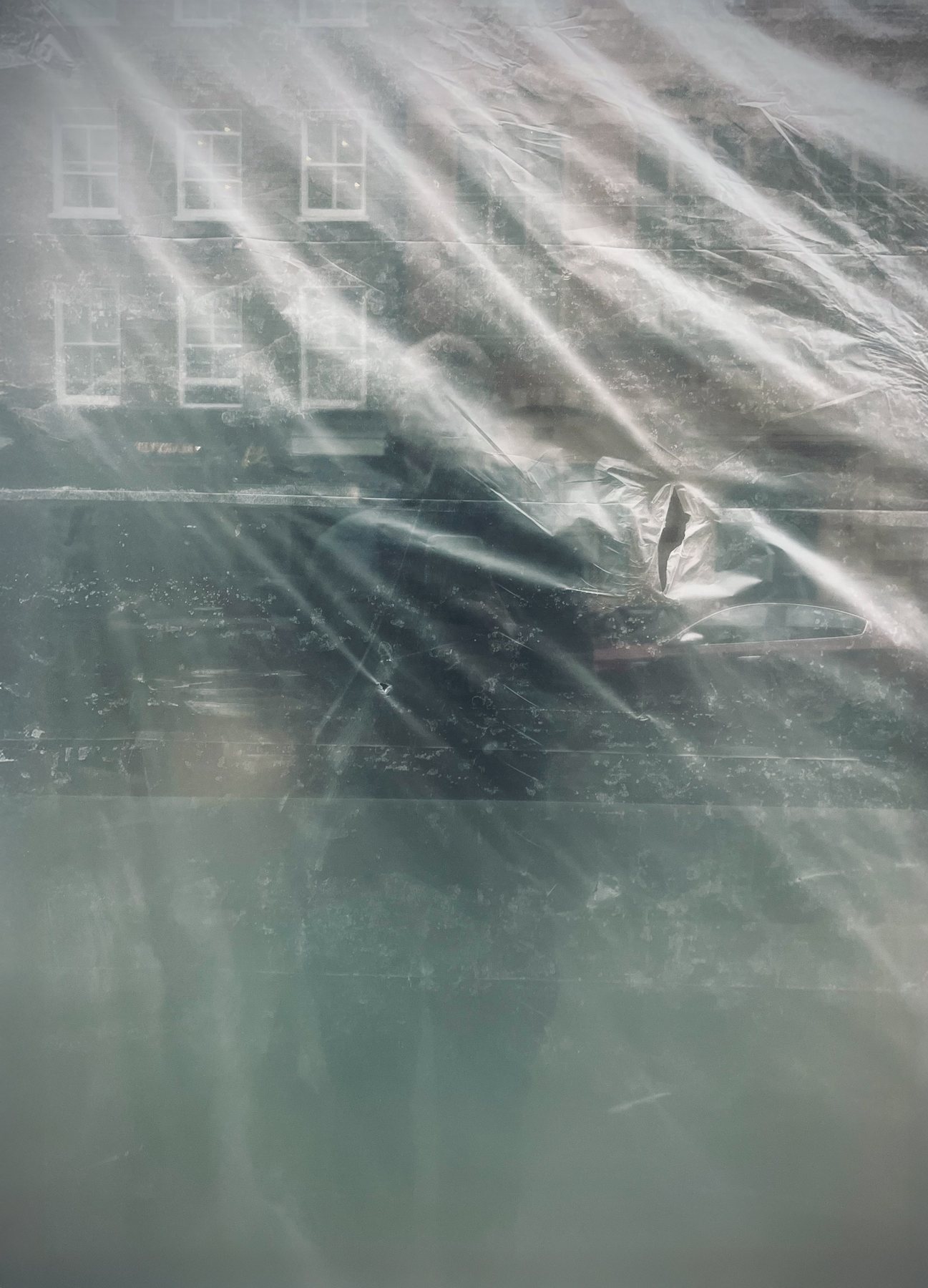 No End In Sight 002: The artist's faint reflection behind crumpled translucent plastic sheeting, with sash windows of a brick building above.