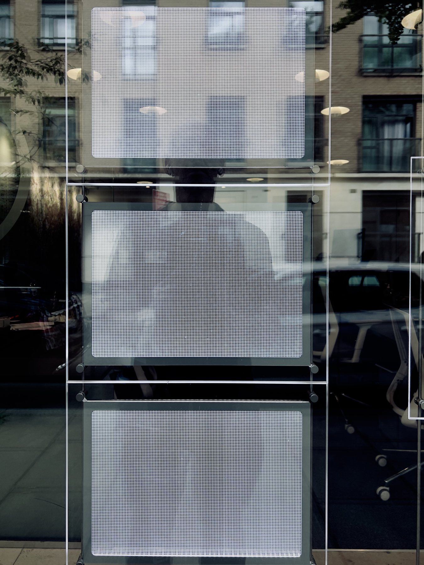 No End In Sight 051: A window with hanging display panels showing blurred reflections of a brick street, the artist's head and torso dimly visible behind them.