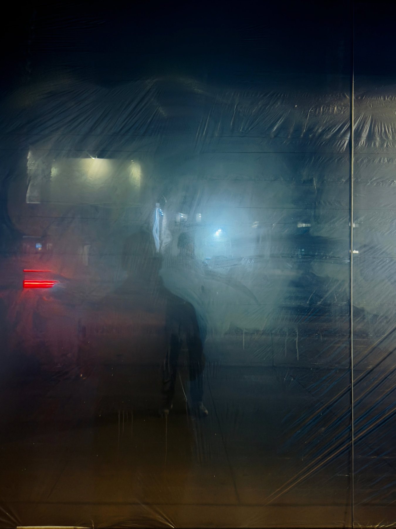 No End In Sight 106: Green: the artist's faint figure reflected in dark plastic-wrapped glass, with a red light and glowing blue haze.