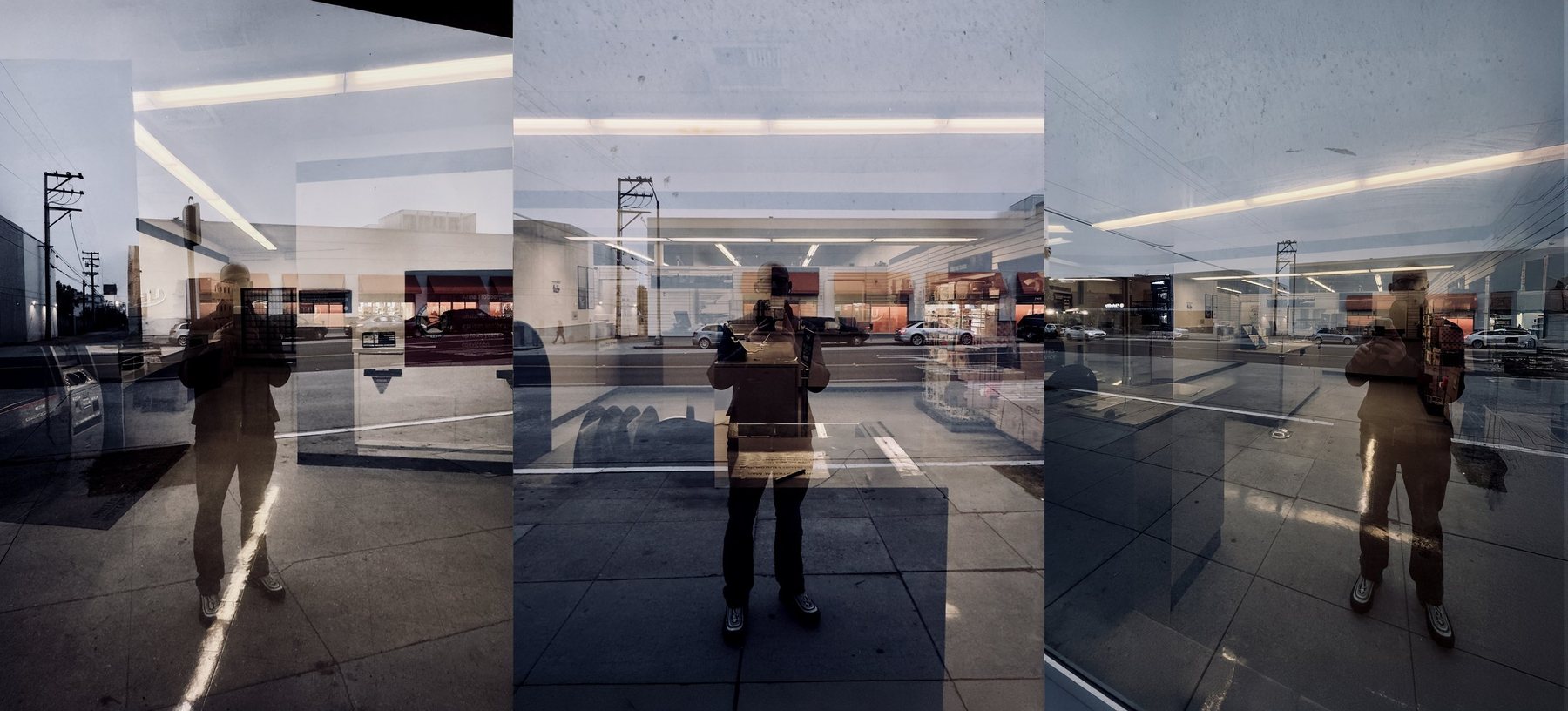 No End In Sight 125: Reflective glass window showing a person taking a photo outside of a storefront, with cars and buildings across the street visible in the reflection.