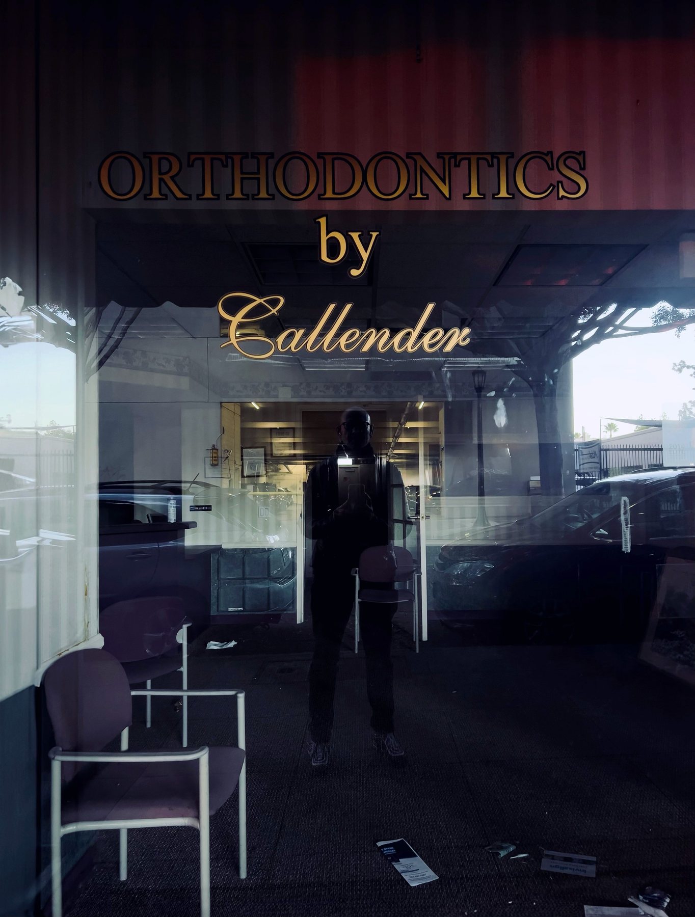 No End In Sight 082: The artist's reflection standing between purple waiting-room chairs behind gold lettering reading ORTHODONTICS by Callender.