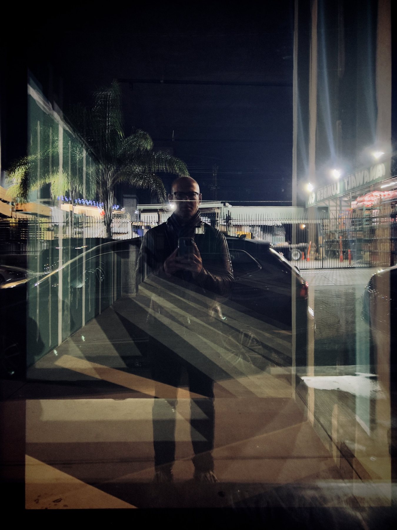 No End In Sight 067: A night scene of the artist with a phone, reflected in glass with palm trees, car headlights, and diagonal striped shadows.