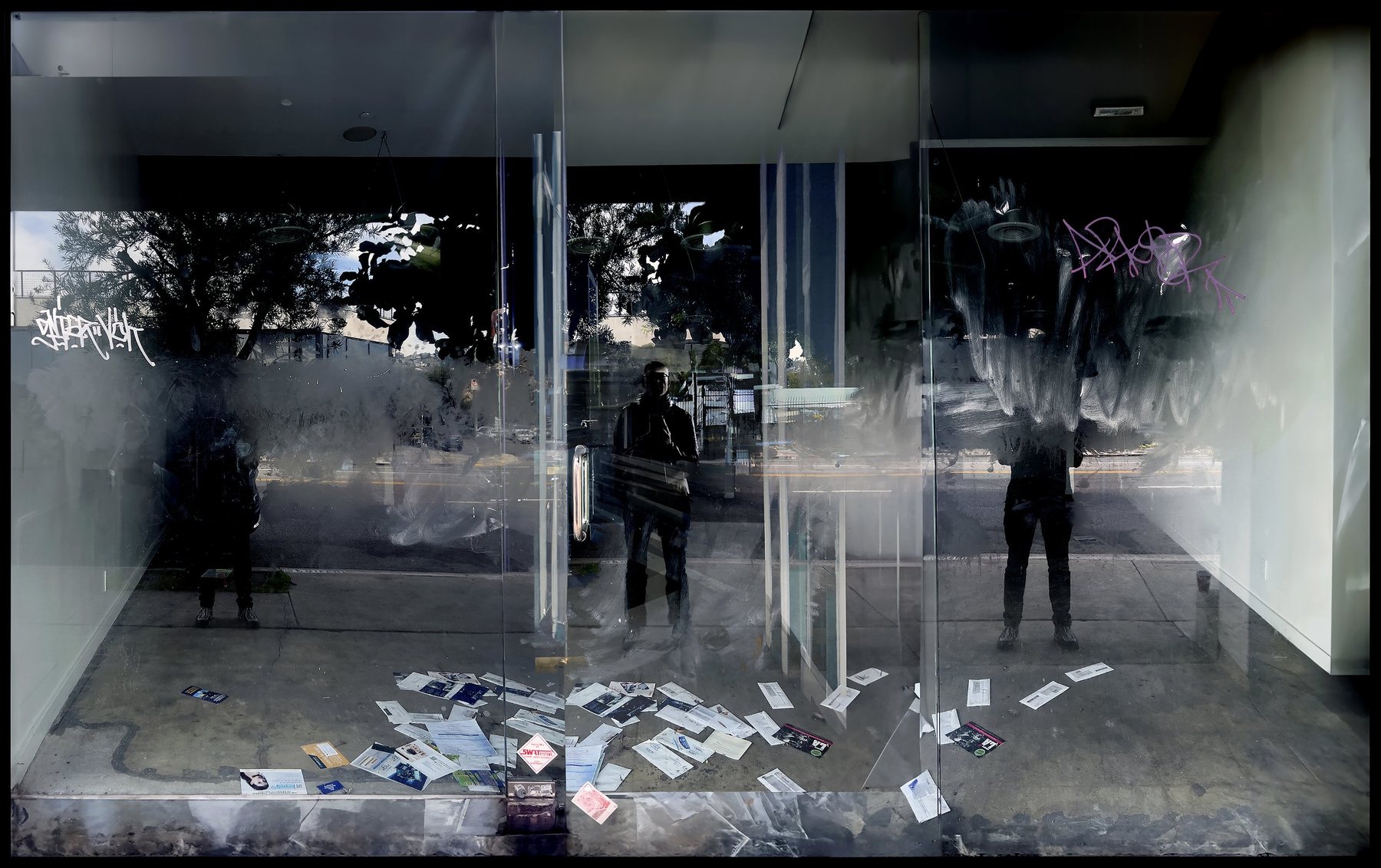 No End In Sight 068: The artist's dark reflection in a shopfront window, with scattered flyers on the floor inside and graffiti above.