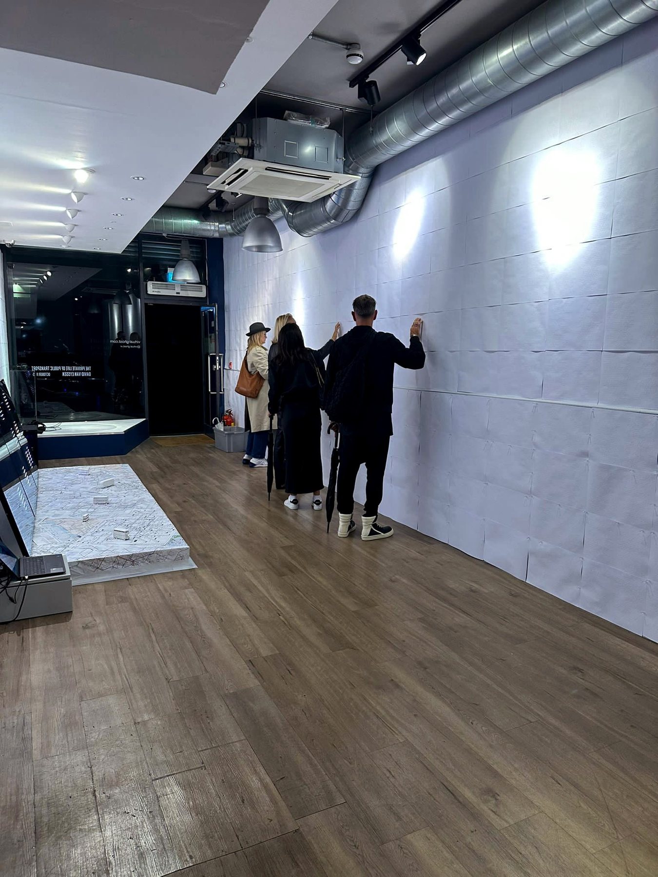 Visitors reach out to touch the white braille-embossed wallpaper in the long gallery, near the map-covered platform.
