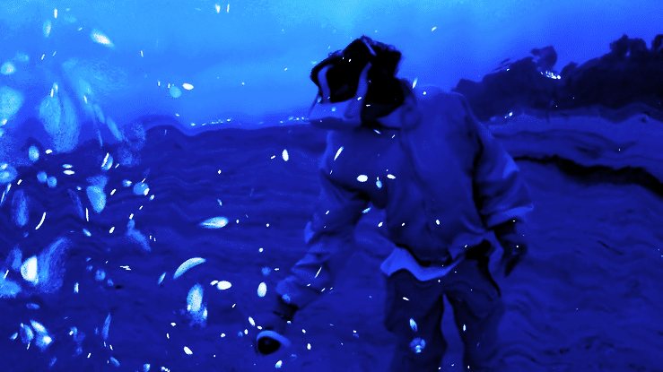 A figure in a hooded jacket and headset leans forward in a saturated blue virtual world of drifting white particles.