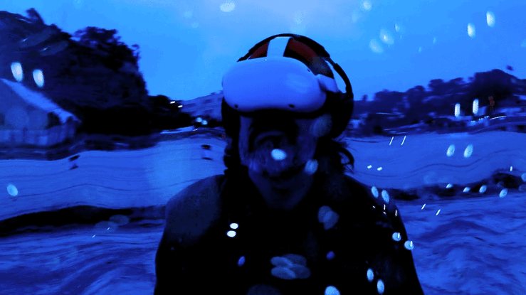 Blue-tinted still of a person in a VR headset and beanie, with water droplets and warped shoreline hills behind, from the Simulations trailer.